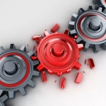 A series of grey cogs connected by a red cog. The red cog has several broken gear teeth, causing the cogs to stop turning